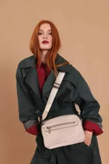 Bandolera de diseño funcional en color beige, confeccionada en material sintético con acabado suave. Presenta un compartimento principal con cierre metálico, bolsillo frontal con cremallera y correa ancha ajustable con logo grabado. Incluye herrajes plateados.