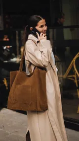 Cartera tipo tote bag de gamuza color marrón, amplia, con doble asa larga para llevar al hombro y bolsillo exterior frontal.