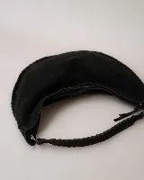 Bolso tipo hobo de gran tamaño, confeccionado en gamuza color marrón oscuro. Presenta un diseño artesanal con costuras visibles y detalles de tientos en el cuerpo, asa integrada con pespuntes a mano y cierre superior.