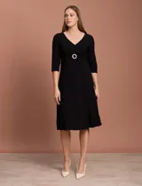 Vestido midi negro de RM Richards en seda fría, con escote en V, mangas 3/4, frunce en la delantera y aplique circular de brillos en el centro.