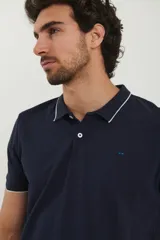 Chomba azul marino de piqué con cuello clásico y tapeta de dos botones. Detalles de ribete blanco en cuello y mangas.