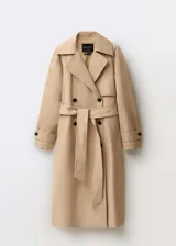 Abrigo tipo trench color beige, de corte oversize y largo hasta la rodilla. Presenta cuello con solapa, cierre frontal cruzado con doble botonadura, cinturón desmontable, dos bolsillos laterales y mangas largas con puños abotonados.