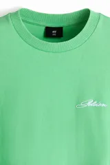 Remera de algodón color verde con cuello redondo acanalado, hombros caídos y bordado pequeño en el pecho con la palabra Golden.