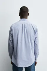 Camisa de corte regular fit confeccionada en tejido de algodón con estampado de rayas verticales. Presenta cuello abotonado, manga larga con puños abotonados y cierre frontal de botones.