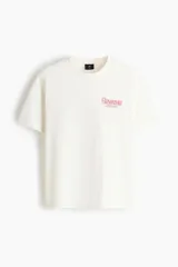 Remera de algodón blanca de corte holgado, con cuello redondo y diseño estampado en el pecho con texto en color rojo.