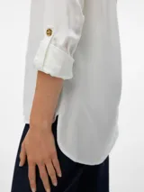 Camisa de color blanco, de mangas largas con opción de vuelta mediante botón, con bolsillo frontal en el pecho, cuello camisero y dobladillo redondeado.