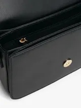 Cartera de hombro negra con solapa frontal y correa ajustable. Presenta un broche metálico dorado con el monograma TH en el centro.