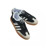 Championes Adidas modelo Samba OG, con diseño clásico de perfil bajo. Presentan una base de gamuza negra con las icónicas tres tiras laterales y puntera en tono crema, finalizando con una suela de goma color caramelo.