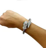 Pulsera rígida plateada con forma de serpiente, con cabeza y cola decoradas con strass y ojos de esmeralda.