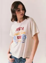 Remera blanca de manga corta y cuello redondo, con estampado frontal de estilo retro con la inscripción "Just a Small Town Girl Journey" acompañada de gráficos florales en tonos rojo, amarillo y azul.