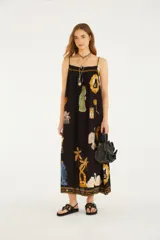 Vestido largo negro de silueta fluida, con finos breteles y detalle fruncido en la parte superior. Presenta un estampado exclusivo con elementos artísticos, palmeras, cisnes y otros motivos.