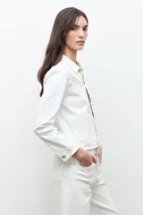 Chaqueta clásica de jean color crudo, con cierre frontal de botones metálicos, bolsillos con solapa en el pecho y cuello camisero.