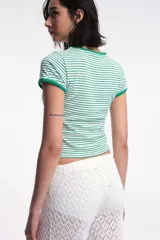 Remera baby blanca de algodón, de corte cropped al cuerpo y mangas cortas. Presenta ribetes negros en contraste en el cuello redondo y los puños, con un estampado localizado de un ají rojo con la inscripción 'Pimentón' en el centro del pecho.