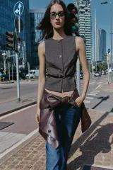 Chaleco jaspeado en tonos grises, con cuello redondo y sin mangas. Presenta cierre frontal con botones dorados y un cinturón fino negro con hebilla dorada.