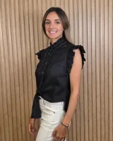 Musculosa de jean celeste sin mangas, con cuello alto fruncido, cierre frontal con botones y detalles de volados en las sisas y a lo largo de la botonera.