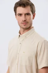 Camisa de manga corta confeccionada en mezcla de lino y algodón, color beige, con cuello camisero abotonado, bolsillo frontal en el pecho y cierre de botones.