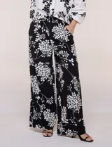 Conjunto de camisa y pantalón amplio con caída fluida. Camisa con escote en V y abotonadura frontal, mangas largas de corte caído con detalle de puntilla calada y puños elastizados fruncidos. Pantalón de tiro alto con cintura elastizada, pierna holgada de corte wide leg con dobladillo ancho en el ruedo y bolsillos laterales.