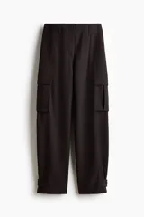 Pantalón cargo de sarga color marrón oscuro, con tiro alto y corte holgado de piernas tipo barrel con pinzas, bolsillos de fuelle con solapa a los lados y trabilla abotonada en el bajo.