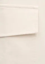 Pantalón recto color blanco crudo, confeccionado en tejido de algodón con elasticidad. Presenta bolsillos de parche con solapa en los laterales de las piernas y cierre frontal de cremallera.
