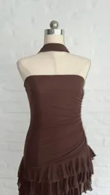 Vestido corto marrón oscuro, estilo strapless, con detalle de frunces en la cintura y falda con volados superpuestos. Incluye un accesorio tipo choker o corbatín a juego.