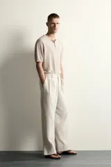 Pantalón relaxed fit de color blanco off-white, confeccionado en tejido con lino. Cuenta con pliegues frontales en la cintura, bolsillos delanteros y cierre frontal con cremallera y botón.