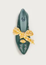 Bailarina de cuero color verde oscuro con detalles de ojales metálicos plateados y lazo desmontable de tela a cuadros amarillos y blancos. Presenta una silueta clásica con punta redondeada y suela plana.