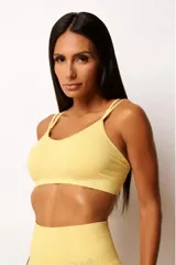 Top deportivo amarillo con textura acanalada, tecnología seamless, breteles finos cruzados en la espalda y abertura interna para copa.