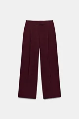 Pantalón de tiro alto color bordó, con pinzas delanteras, bolsillos frontales y falsos bolsillos con solapa en la espalda. Tiene pernera ancha y cierre frontal con cremallera, botón interior y gancho.