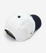 Gorra blanca de sarga con visera azul marino y bordado de Snoopy jugando baseball.