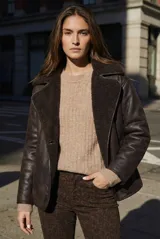 Campera tipo gamulan de corte oversize, color marrón oscuro con interior y solapas de corderito al tono. Presenta cierre frontal y mangas largas.