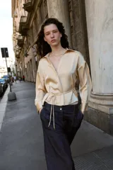 Camisa de manga larga color beige claro, con cuello solapa, escote pico y detalle de cinturón fino a tono que se anuda en la cintura.