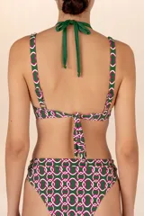 Top de bikini verde oscuro con estampado geométrico en rosa y blanco. Diseño halter con tiras al cuello y aro circular central.