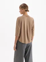 Remera de silueta relajada confeccionada en tela de punto suave. Presenta escote redondo, mangas 3/4, recorte estratégico en la espalda y tajos laterales que aportan movimiento y una caída fluida.