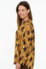 Camisa de manga larga con estampado geométrico de formas orgánicas en tonos mostaza, marrón y negro. Presenta cuello clásico y cierre frontal con botones.