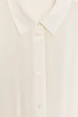 Vestido mono corto de gasa color crudo, con cuello solapa, cierre frontal de botones y manga larga con puños. Presenta cintura elástica y falda con diseño de volantes superpuestos en el bajo.