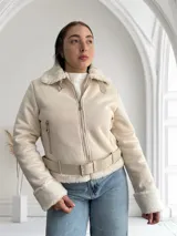 Chaqueta color crema con cuello y puños de piel sintética, cierre frontal con cremallera y cinturón ajustable en la cintura.
