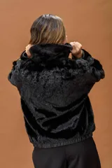 Campera tipo bomber de piel sintética negra con textura aterciopelada. Presenta capucha, cierre frontal con cremallera metálica y detalles en cuero sintético en la zona del cierre y los puños.