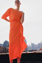 Vestido midi color naranja de la colección ZW de Zara, con cuello redondo, manga corta y detalle de tejido drapeado con volados en el delantero. Cuenta con cierre en la espalda con abertura y botón.