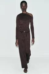 Pantalón de tiro alto y pierna recta, confeccionado en tejido piqué color beige. Presenta cintura elástica y un cinturón fino a contraste en color negro con detalle de pieza metálica central.