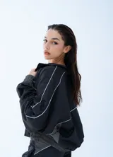 Campera rompeviento negra de estilo deportivo, con cierre frontal completo, cuello alto y detalles de líneas blancas en los hombros y mangas. Presenta puños y cintura elásticos en tono gris oscuro.