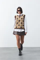 Chaleco tejido sin mangas con diseño de rombos tipo argyle en tonos marrón y beige, con cuello redondo y terminaciones acanaladas.