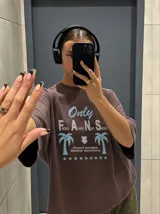 Remera oversize marrón con estampado gráfico frontal en tonos celestes y blancos con la leyenda "Only Fans", palmeras y estrellas.