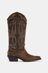 Bota estilo cowboy de piel con efecto desgastado. Presenta bordados decorativos en el cuerpo, doble tirador lateral y tacón medio con acabado en punta.