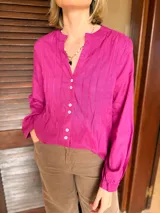 Camisa de manga larga en color fucsia, con cuello mao y cierre frontal de botones. Presenta detalles de alforzas verticales en el frente y puños abotonados.