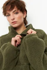 Buzo negro de teddy con cuello alto y cierre de cremallera parcial. Presenta bolsillos de nylon en la parte inferior delantera.