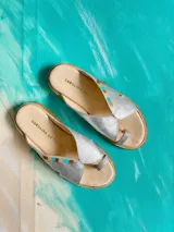 Sandalias de cuero plateado metalizado, con diseño de tira al dedo y detalles pintados a mano en el empeine. Poseen suela plana con borde texturizado de yute.