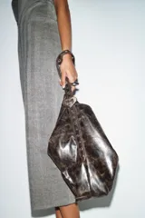 Bolso de hombro formato shopper con acabado efecto cuero desgastado. Cuenta con asa ajustable mediante hebilla metálica y detalle de tachas, cierre principal mediante imán y bolsillo interior con cremallera.