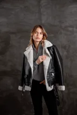 Campera tipo gamulán de eco cuero negro con interior y solapas de corderito sintético en color crudo. Presenta cierre frontal, bolsillos laterales con cierre y cinturón ajustable en la cintura.