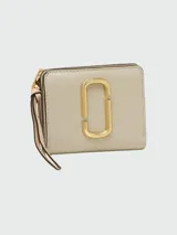 Billetera mini compacta Marc Jacobs color beige con logo dorado en el frente y correa de muñeca rosa.