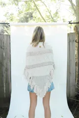 Poncho de tejido de algodón color beige claro, con diseño de punto calado y flecos en el borde inferior.